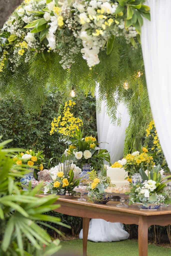 mesa de madeira com bolo de casamento e arranjos com flores brancas amarelas e azuis