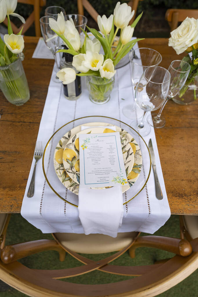mesa de madeira posta com prato com estampa floral amarela e menu sobre o prato