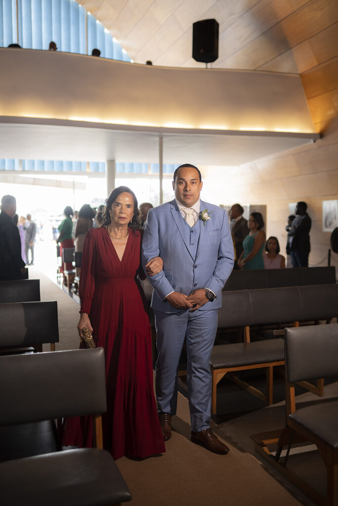 entrada do noivo com tenro azul ao lado de mulher com vetsido vermelho escuro com decote em v