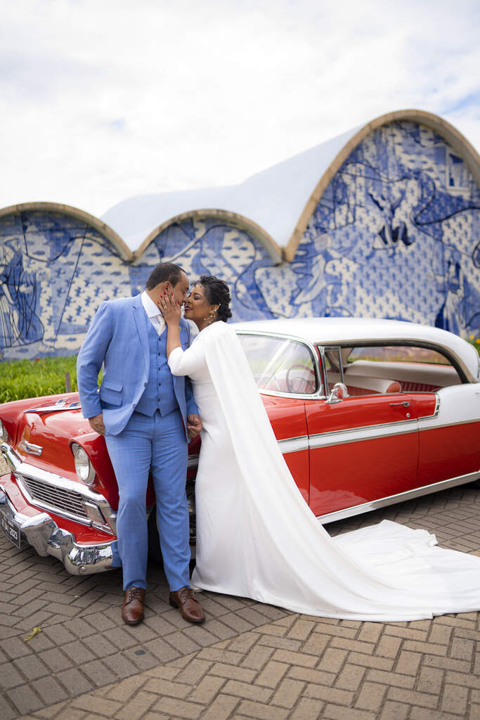 noivos se beijando na frenet de carro antigo vermelho e branco na frente da igreja da pampulha