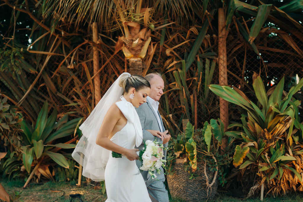 entrada da noiva segurando buquê com flores brancas ao lado do pai com terno cinza