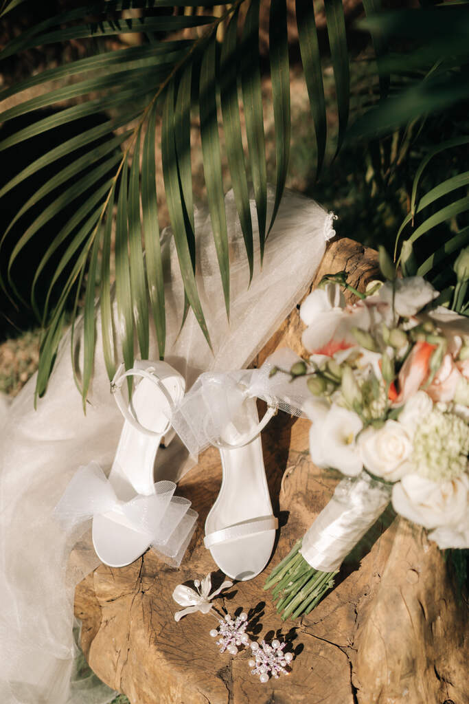 sandália branca com laço na ponta e ao lado véu e buquê com flores brancas