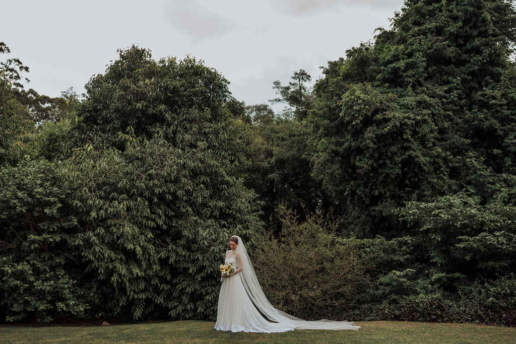 noiva com vestido com cauda média e véu catedral segurando buquê com flores brancas e girassois ao ar livre