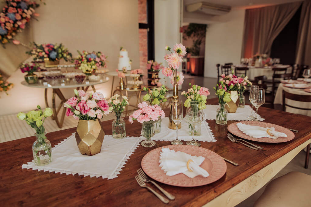 mesa de madeira posta com prato cor de rosa e vasos com flores brancas e rosas
