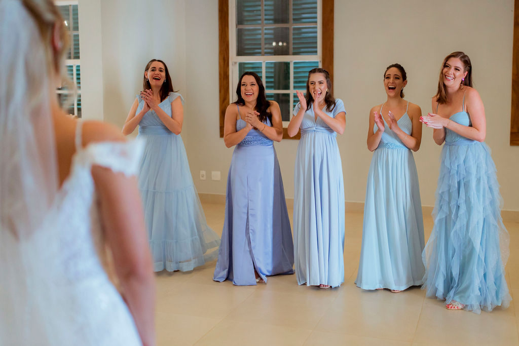 cinco madrinhas com vestido azul serenity sorrindo durante o first look com a noiva no salão