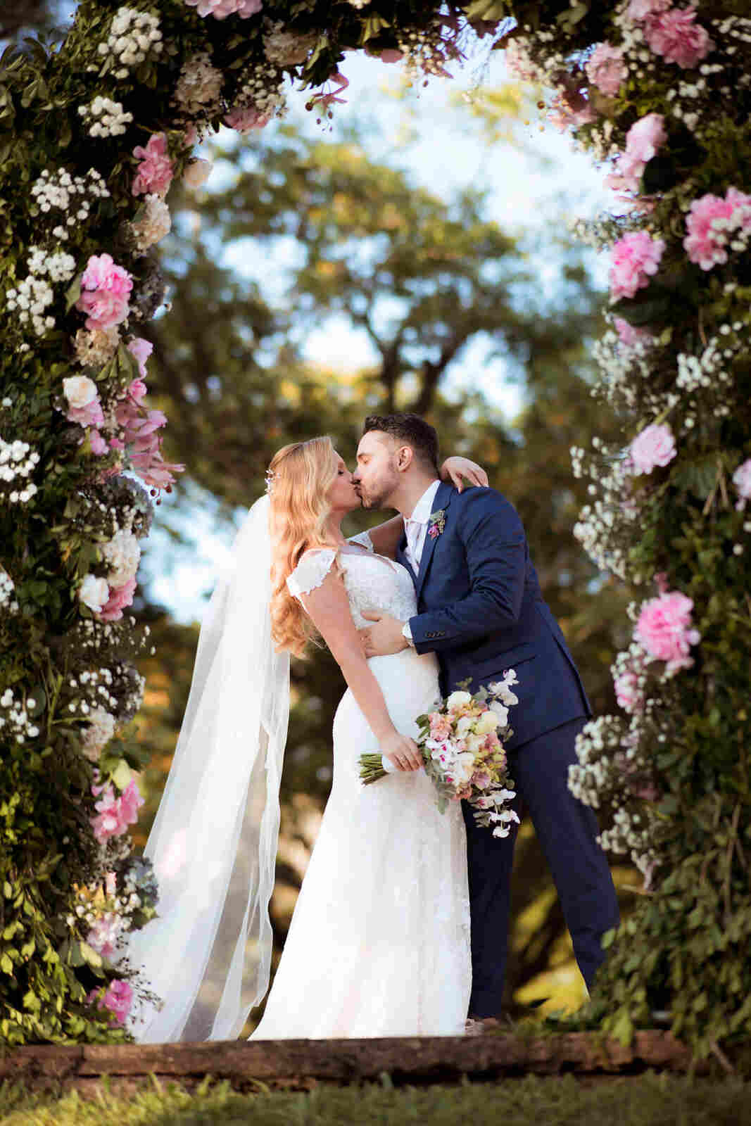 noivos se beijando sob altar florido branco e rosa
