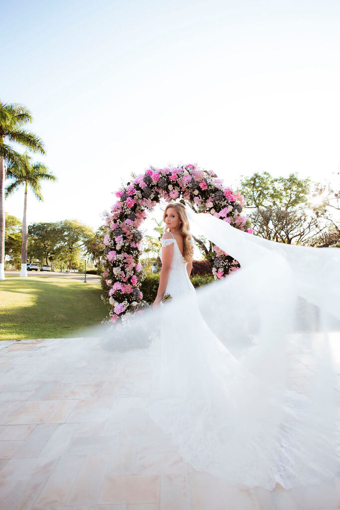 noiva com véu longo sob altar floral branco e rosa