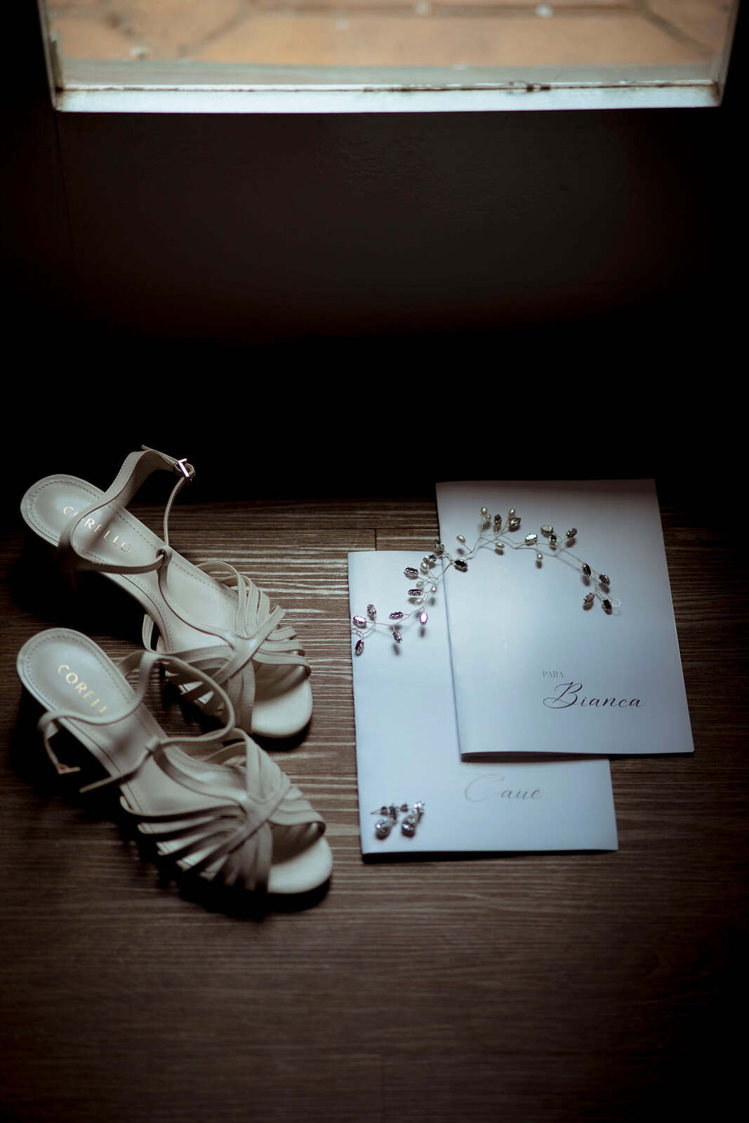 sandália branca com tiras ao lado de dois cadernos de votos brancos e minimalistas e grinalda com pedras