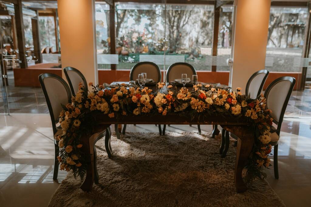 mesa comunitária com arranjo de flores amarelas e laranjas dentro do salão
