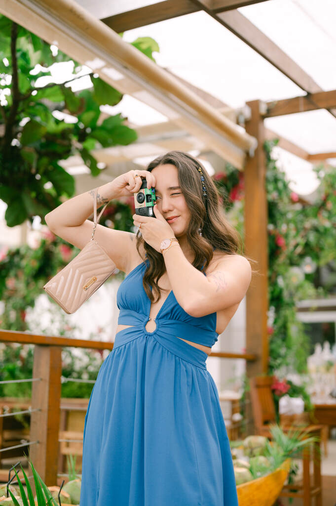 convidada de casamento azul com recortes tirando foto com câmera analógica