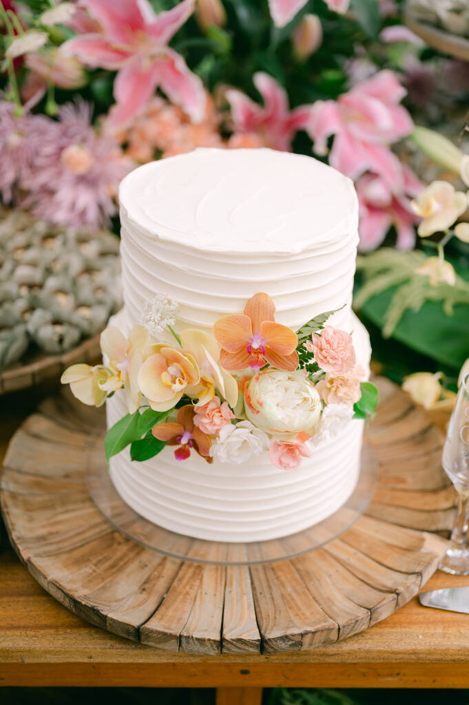 bolo de casamento espatulado com dois andares com flores brancas amarelas rosas e laranjas sob bandeja de madeira