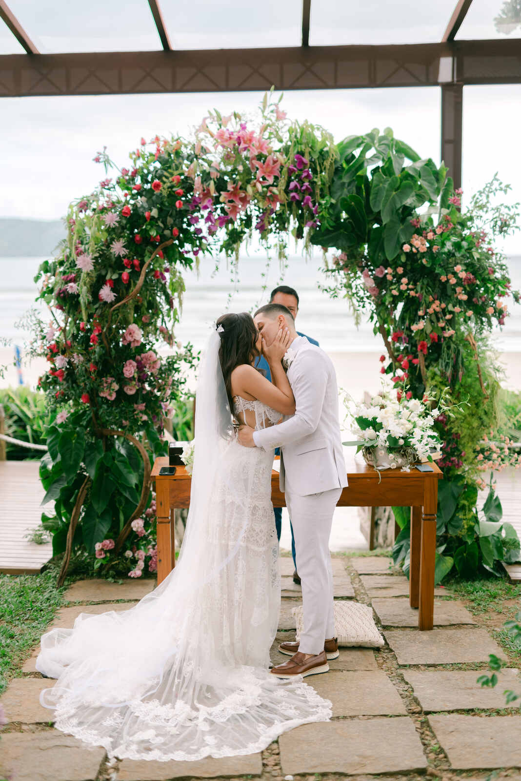 noivos se beijando no altar com plantas e flores rosas com vista para praia