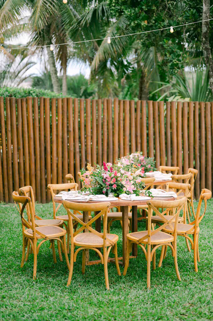 mesa de madeira decorado com plantas e flores cor de rosa e atrás cercad e bambu no jardim