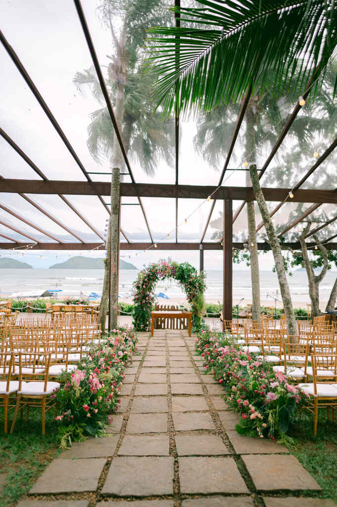 cadeiras de madeira no estilo tiffany decorado com plantas e flores rosas em salão com telhado transparente com visão para praia