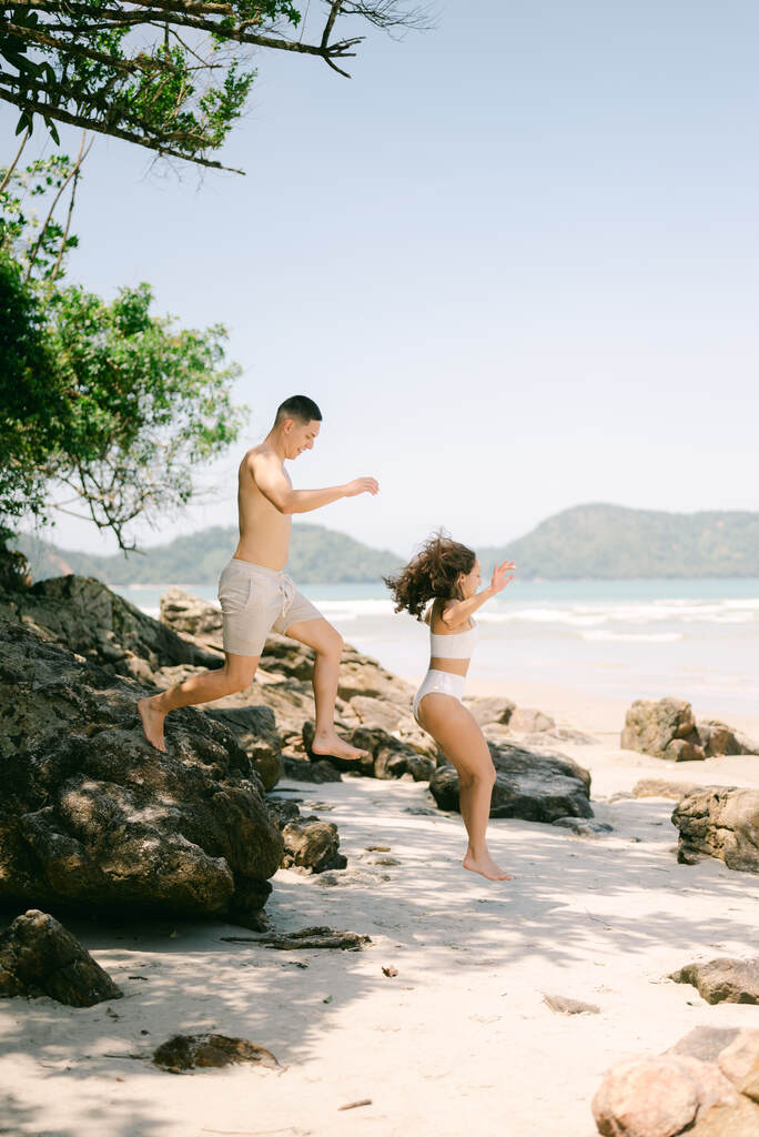 casal com roupa de praia pulando de pedra