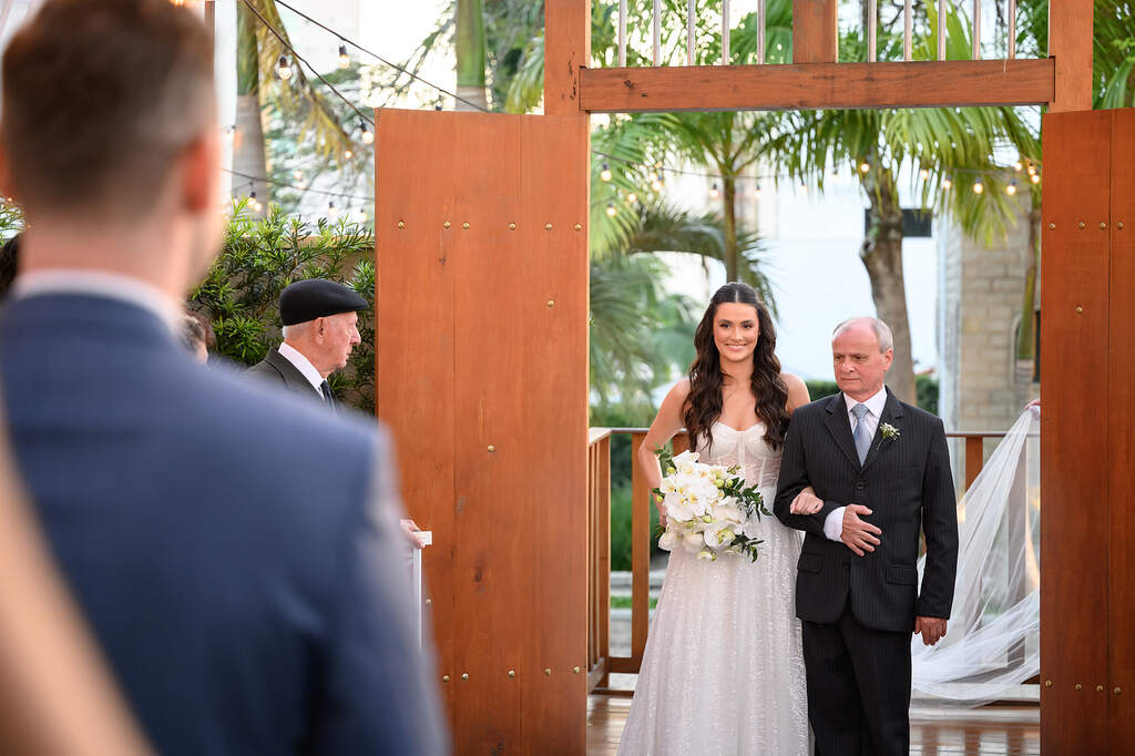 entrada da noiva com buquê branco ao lado dopai com terno preto