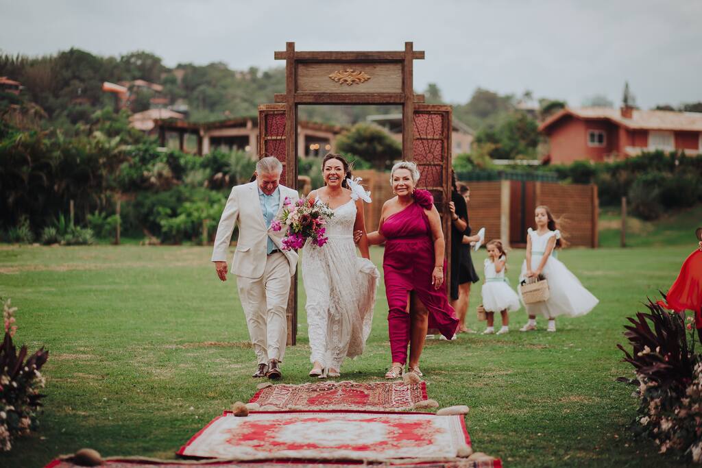 entrada da noiva ao lado do pai com terno bege e mãe com vetsido na cor fúcsia
