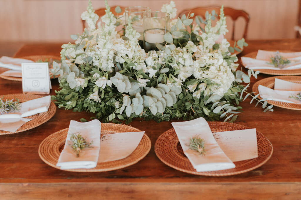 mesa de madeira posta e flores brancas com ramos de eucaliptos no centro