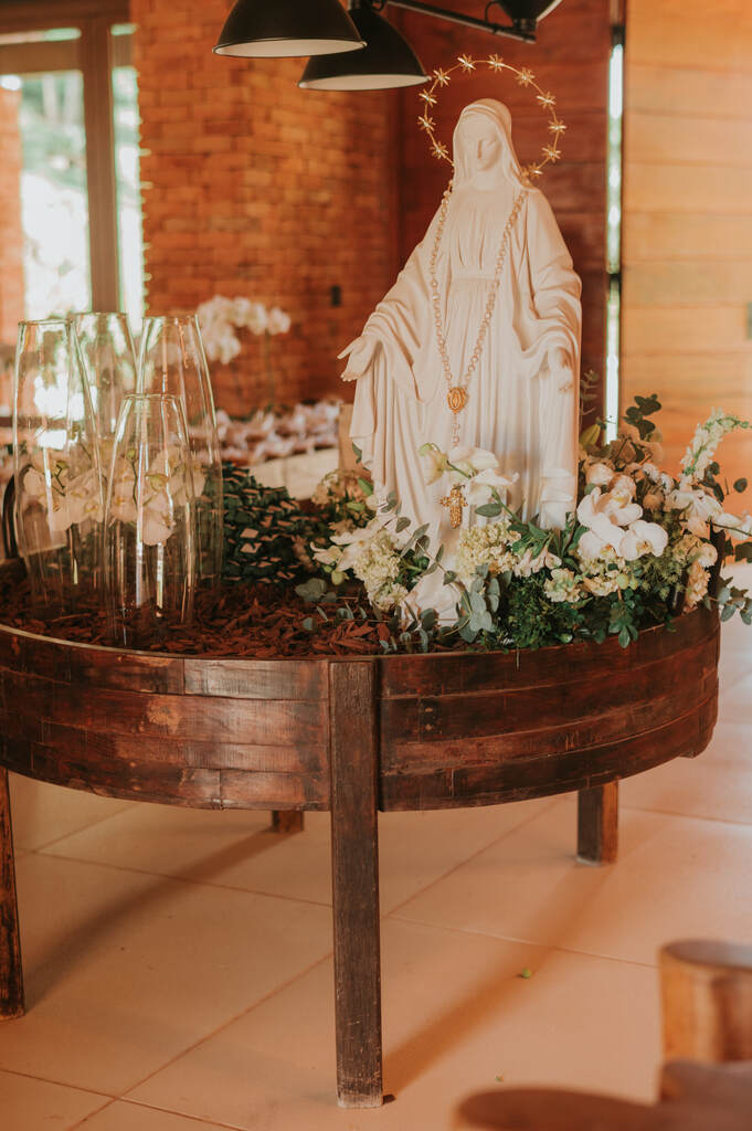 mesa redonda de madeira com vasos com flores e estáttua de santa em gesso