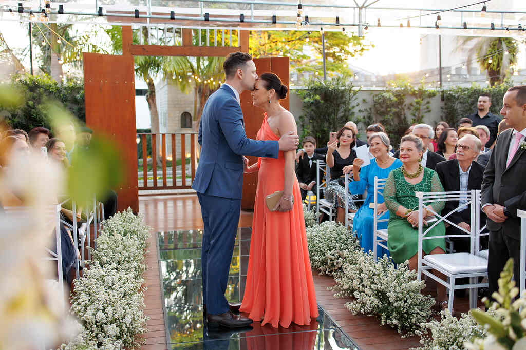 entrada do noivo com terno azul beijando a testa da mãe com vestido laranja