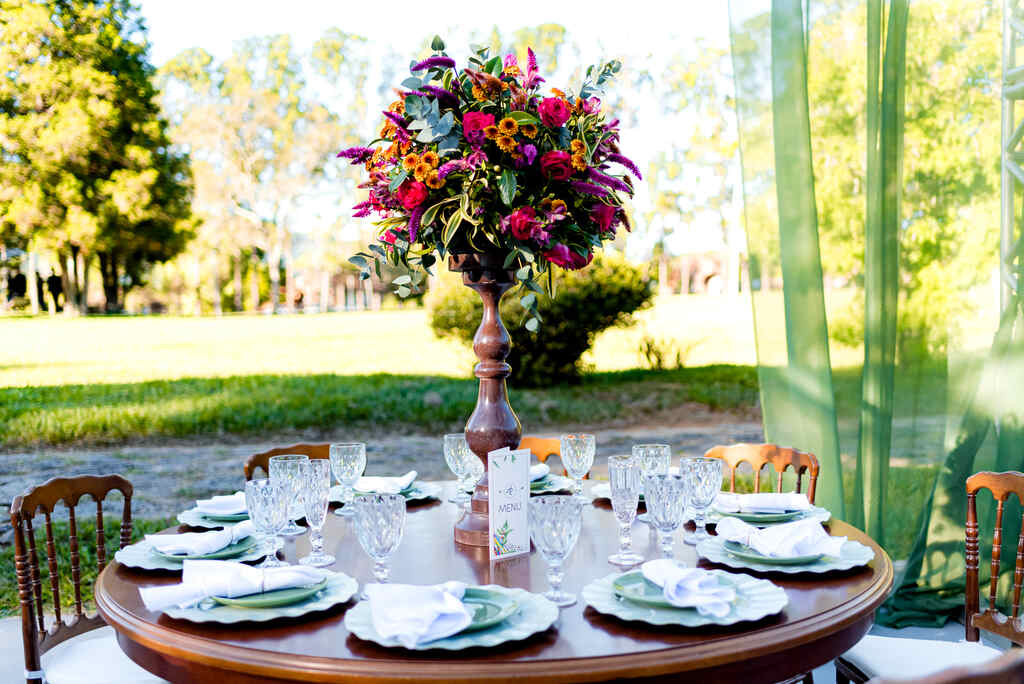 mesa redonda de madeira com mesa posta com vaso com flores rosas amarelas e roxas