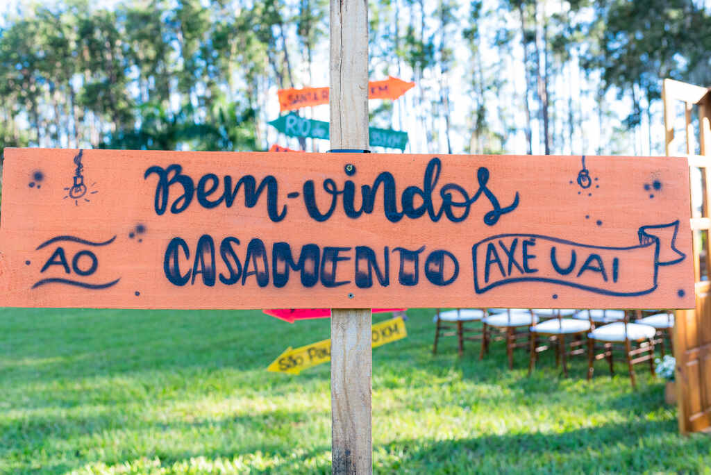 placa de madeira laranja escrito em letras azuis bem-vindos ao casamento axé uai 