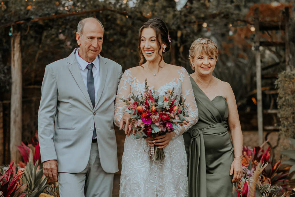 noiva ao lado do pai com tenro cinza e gravata cinza escuro e mãe com vestido verde oliva