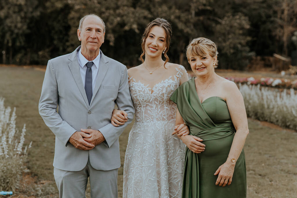 noiva ao lado do pai com tenro cinza e gravata cinza escuro e mãe com vestido verde oliva