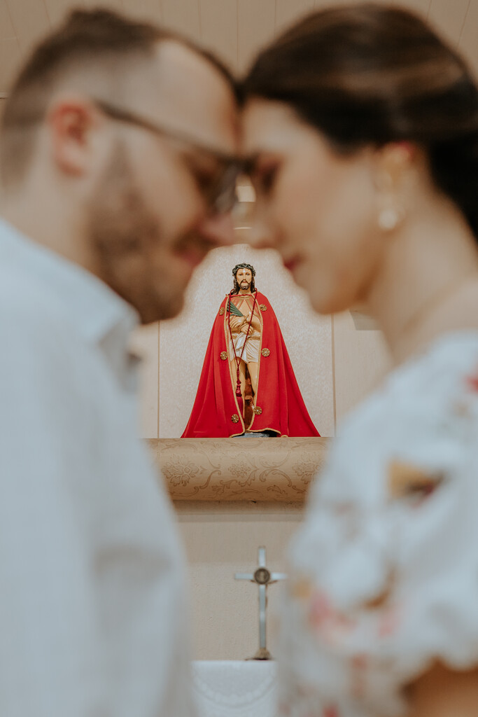 noivos abraçados e ao fundo estátua de santo catolico