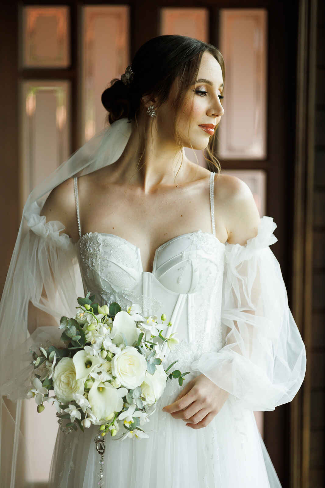 mulher com cabelo pres com véu e vetsido de noiva com corset e manga removivel e bufante segurando buquê com rosas brancas