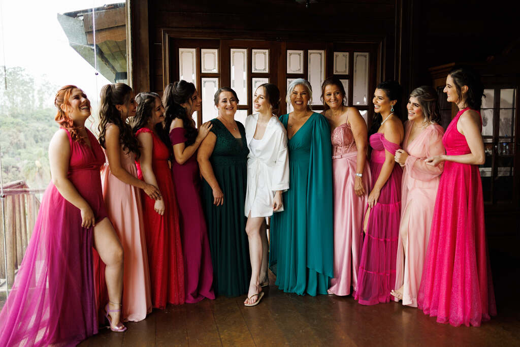 noiva com robe branco ao lado das madrinhas com vestidos cor de rosa e mães com vestidos verdes