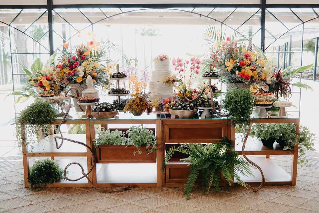 mesa de madeira com bolo de casamento com arranjos com flores e plantas
