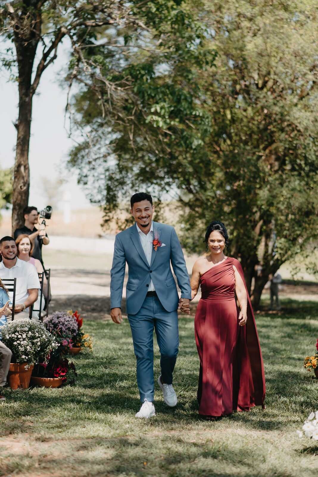 entrada do noivo com tenro azul de mãos dadas com a mãe com vestido marsala