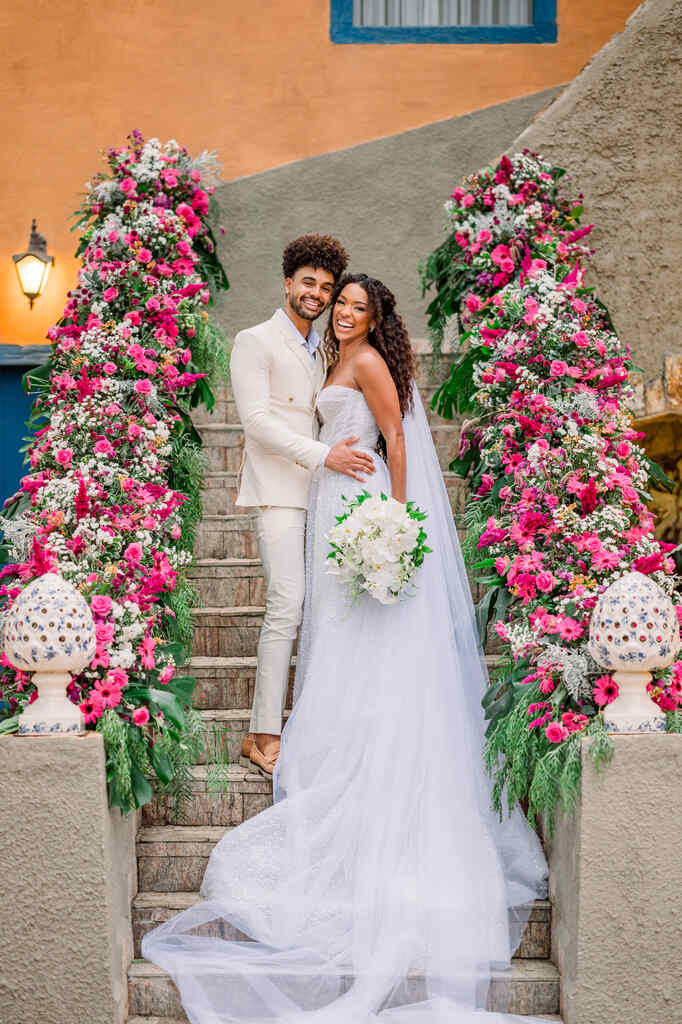 noivos se abraçando na escada decorada com flores brancas e rosas