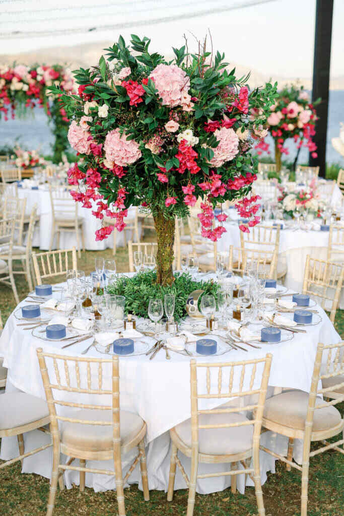 mesa redonda posta com pratinhos azuis e grande arranjo com flores rosas no centro