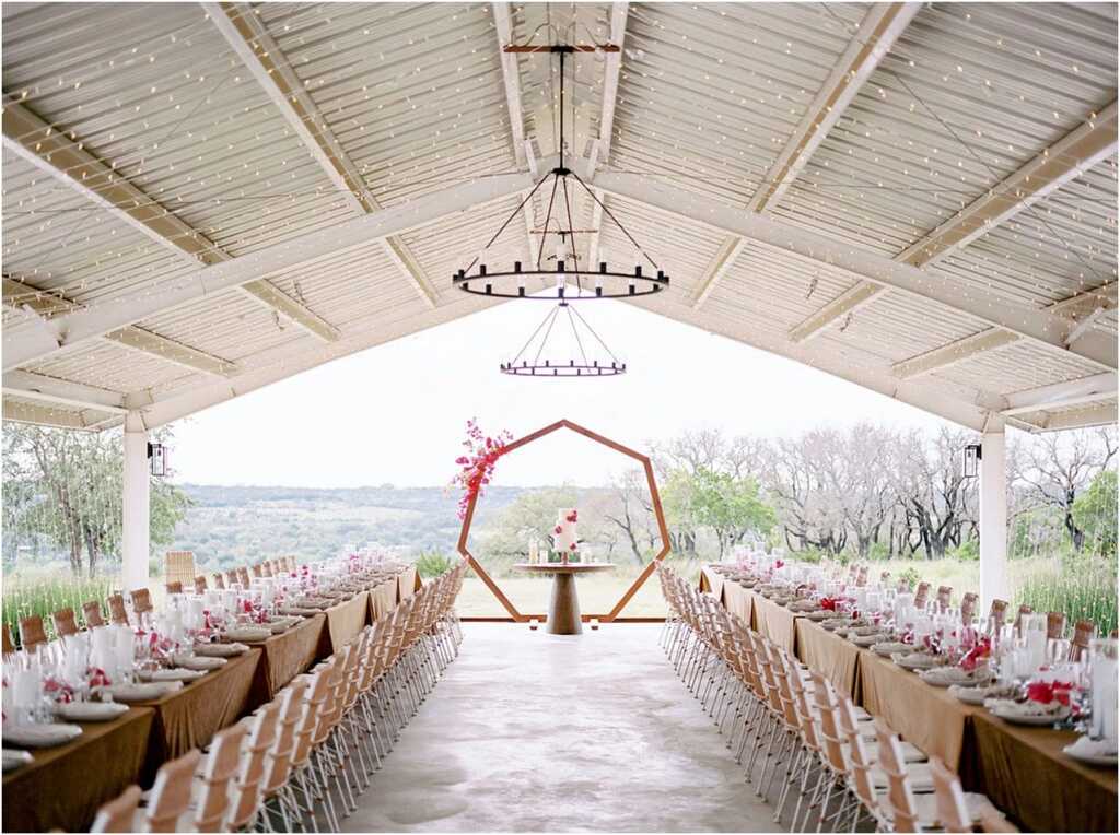 salão com visão para o campo com duas fileiras com mesas comunitárias e no centro altar moderno com flores fucsia