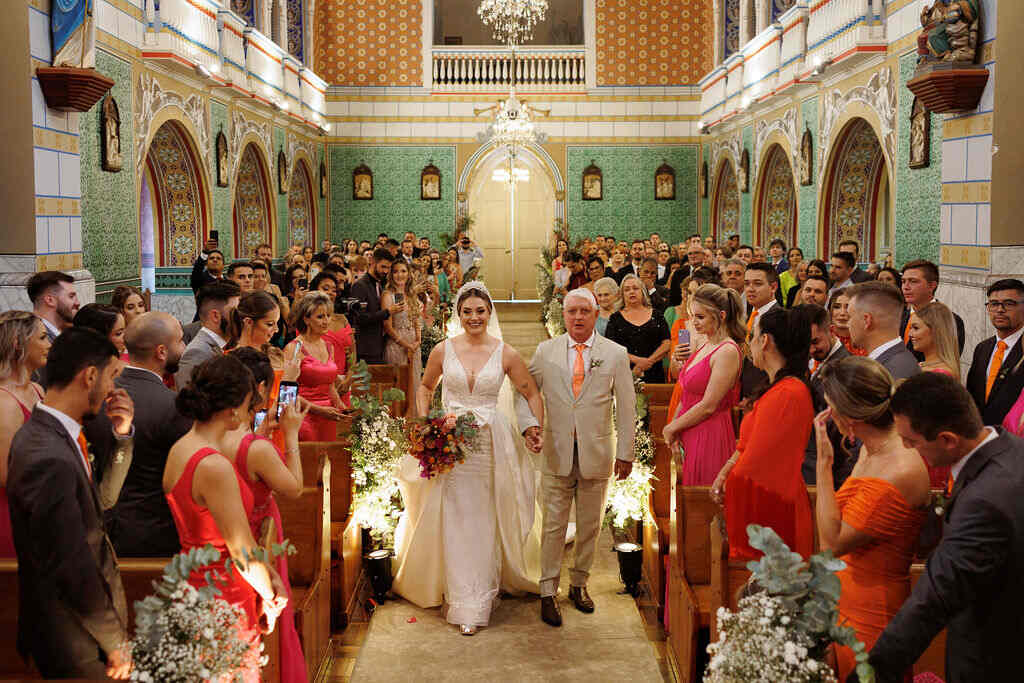 entrada da noiva de mãos dadas com o pai com tenro off white e gravata laranja na igreja