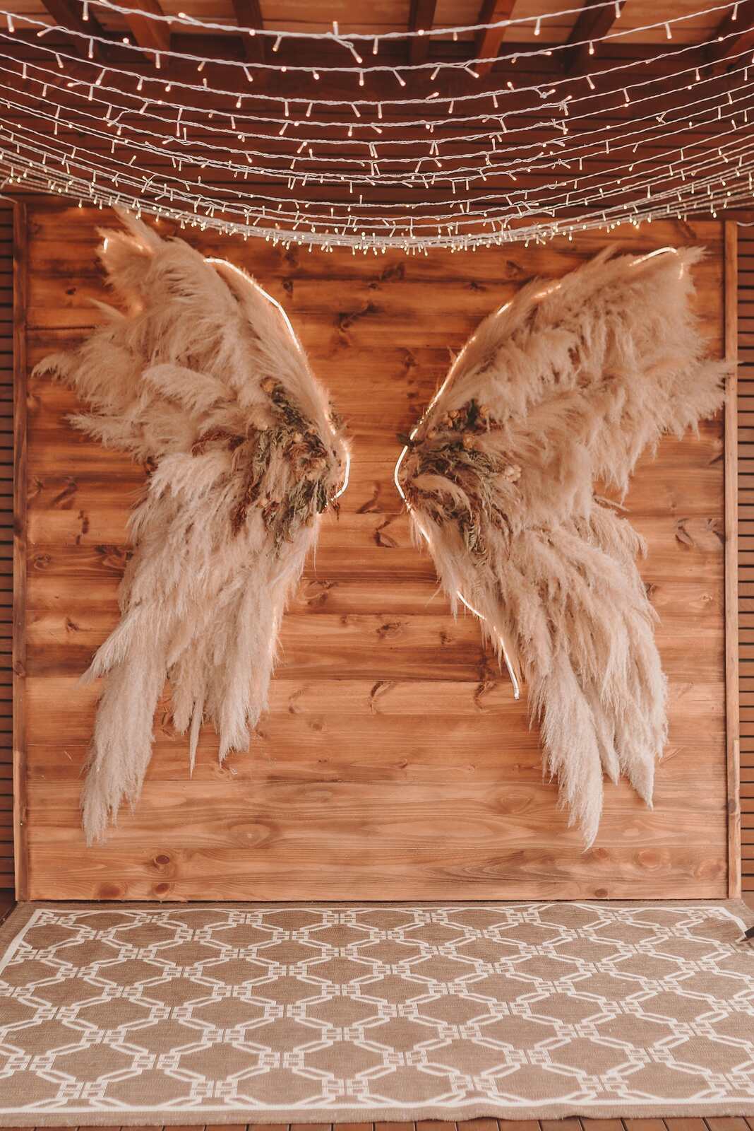 painel de madeira com asas feitas de capim de pampas e varal de luzinhas