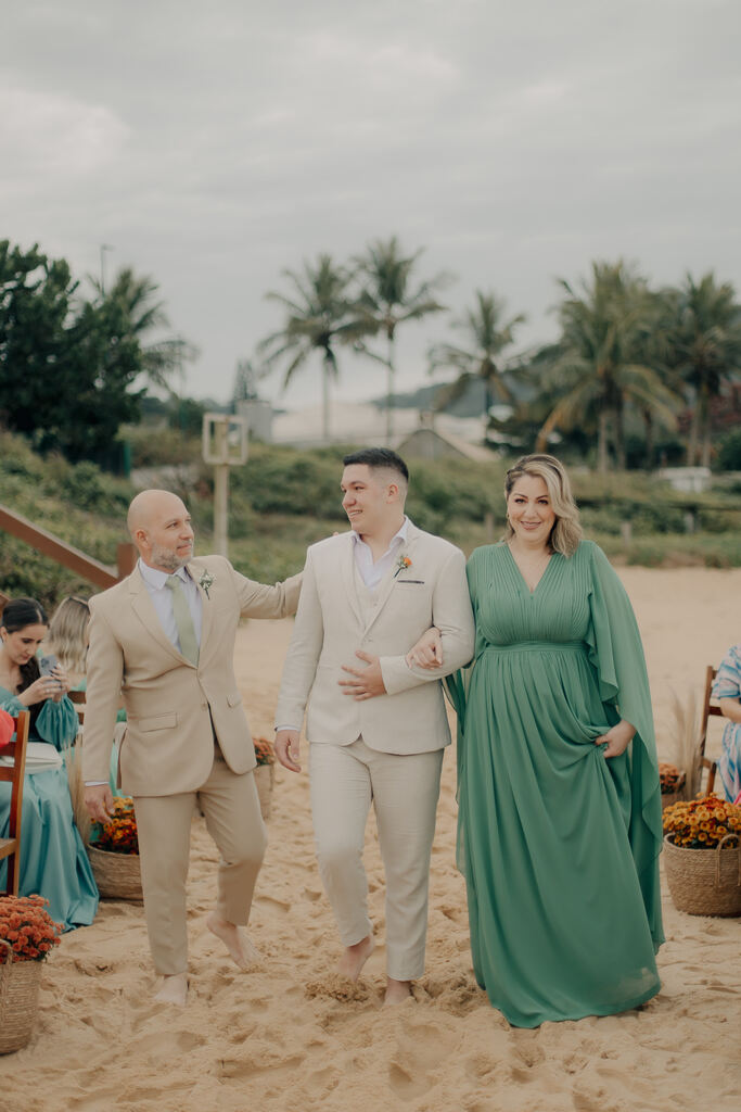 entrada do noivo cm terno off white ao lado do pai com tenro bege e mãe com vestido verde com decote em v