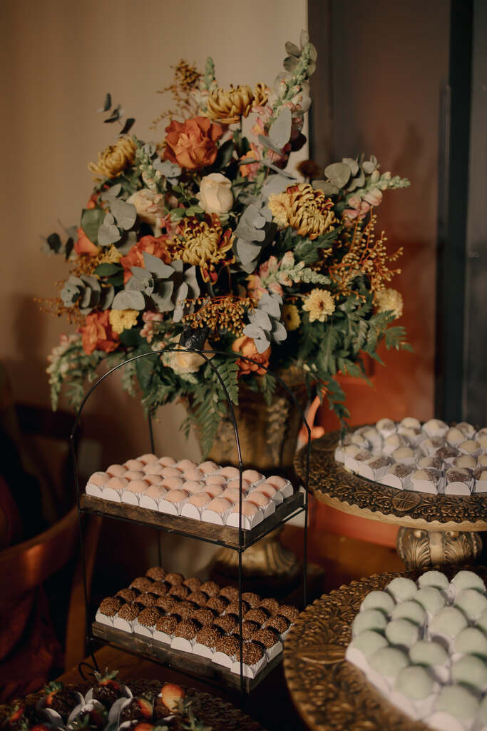 bandejas de doces de casamento e vasos com flores amarelas e laranjas com folhas de eucalipto
