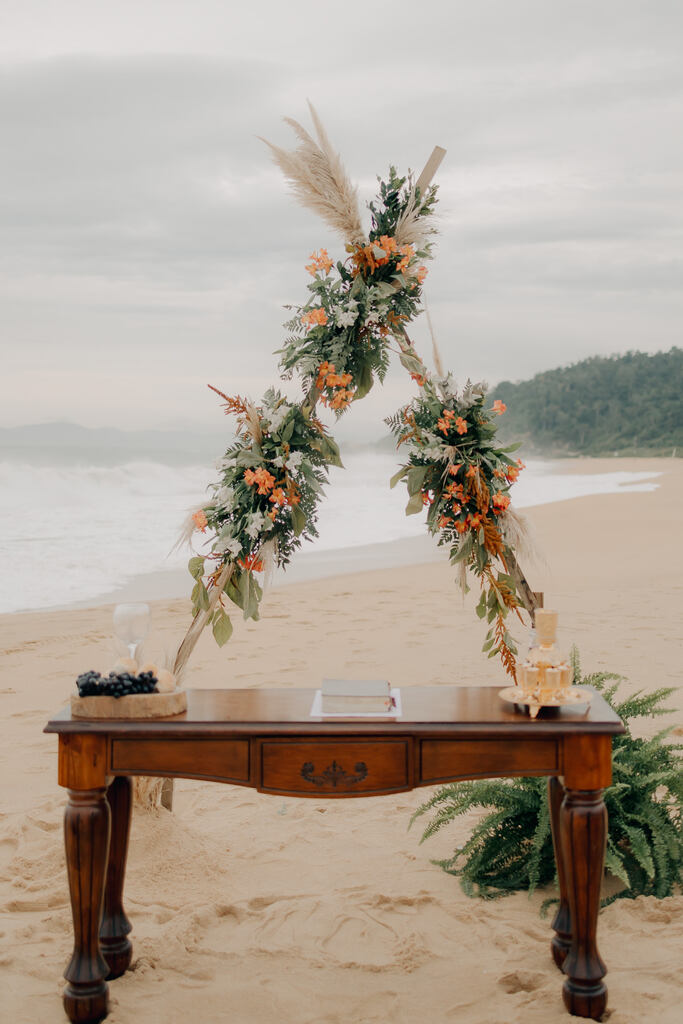 mesa de madeira antiga e altar triangular com capim dos pampas e flores brancas e laranjas na praia