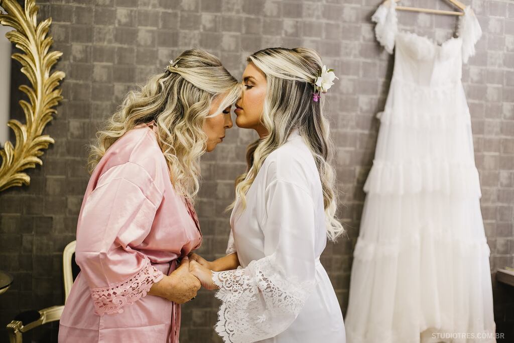 noiva com robe branco beijando a testa da mãe com robe cor de rosa