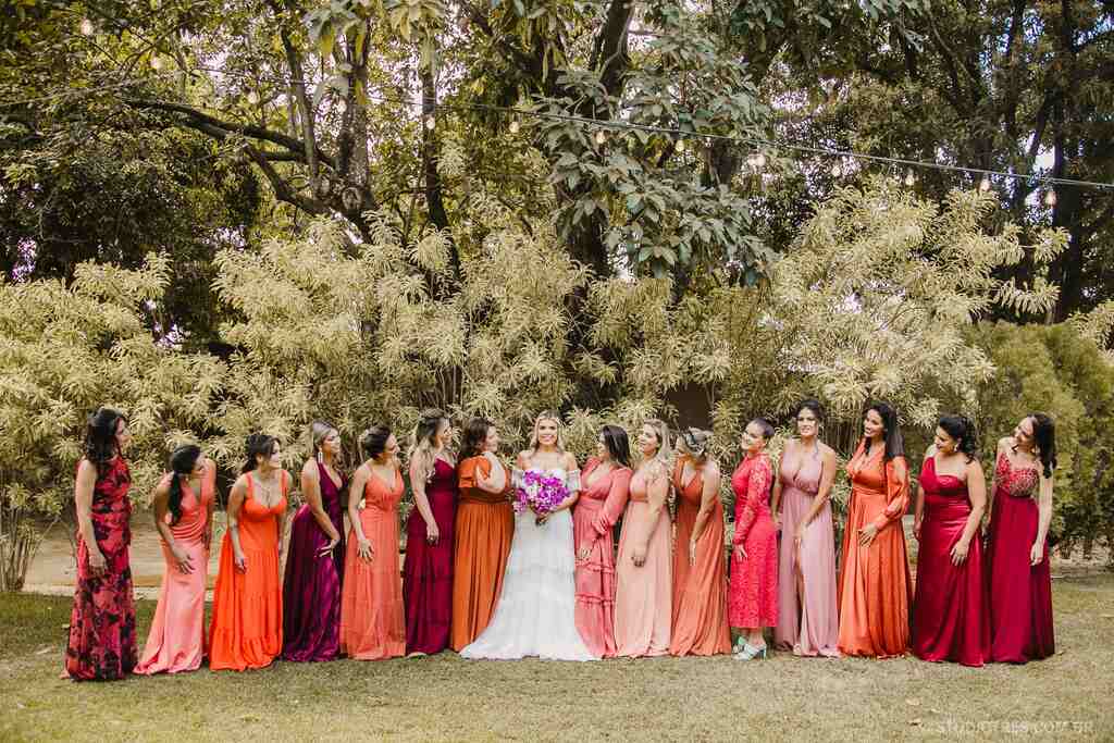 noiva segurando buquÊ roxo ao lado das madrinhas com vestidos rosas laranjas e vermelhos