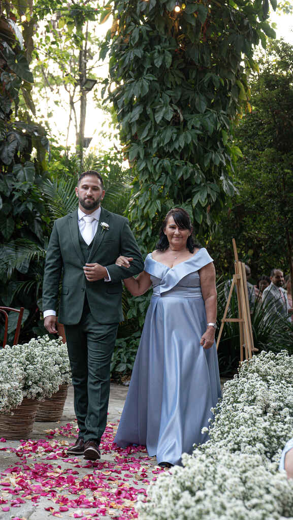 entrada do noivo com terno verde e gravata branca ao lado da mãe com vestido azul serenity