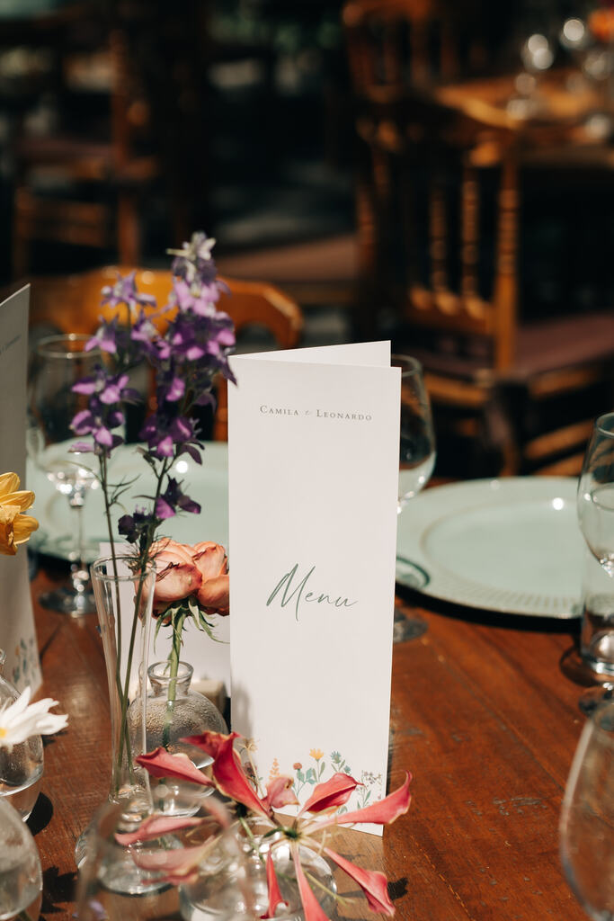 menu de casamento branco e minimalista no centro da mesa ao lado de flores coloridas