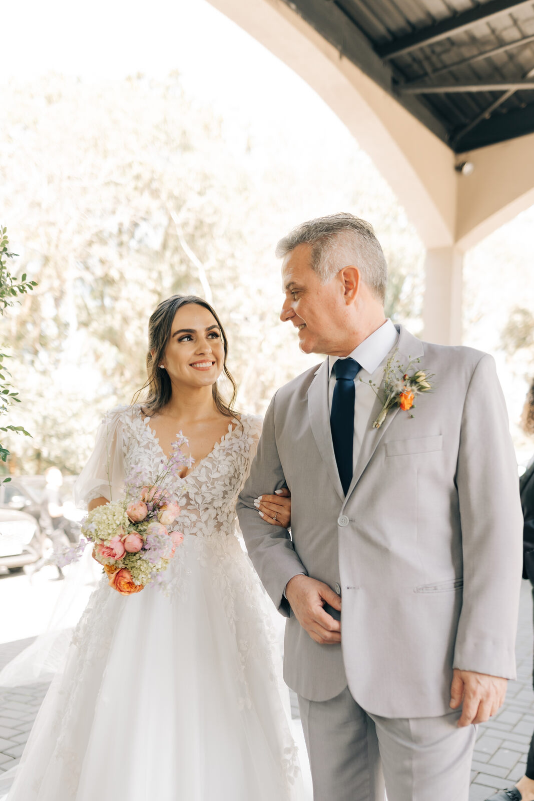 entrada da noiva com o pai com terno cinza com gravata azul e lapela com flor laranja