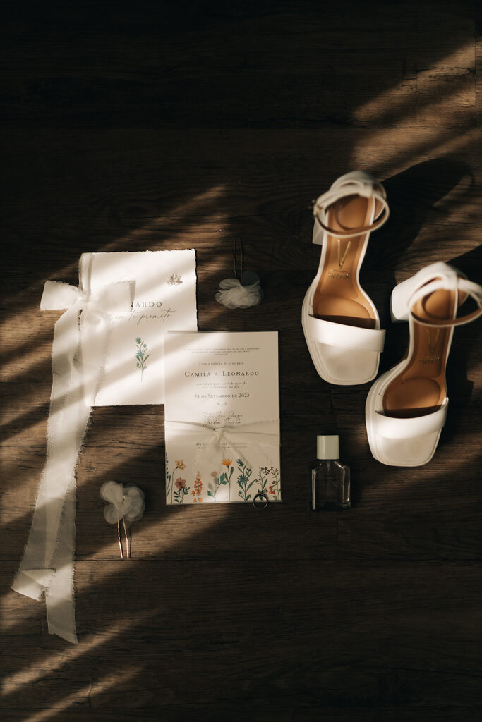 sandália branca com salto baixo ao lado de convite de casamento branco com estampa floral