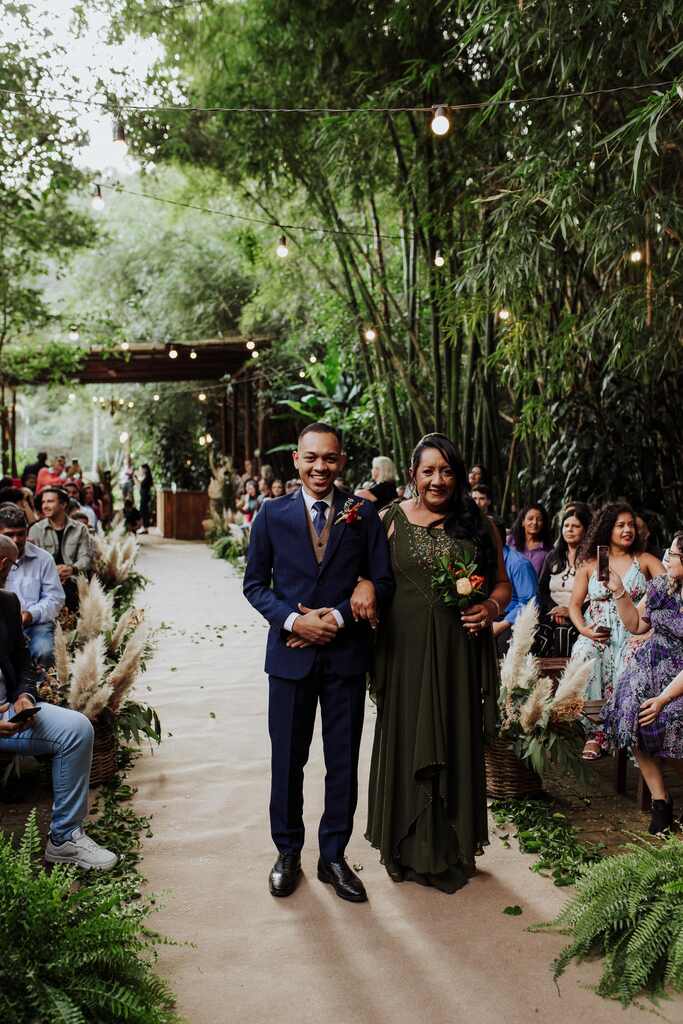 entrada do noivo com terno azul ao lado da mãe com vestido verde escuro