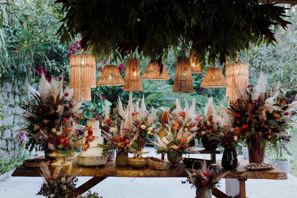 mesa de madeira rústica ao ar livre com bolo de casamento com vasos com capim dos pampas e flores 