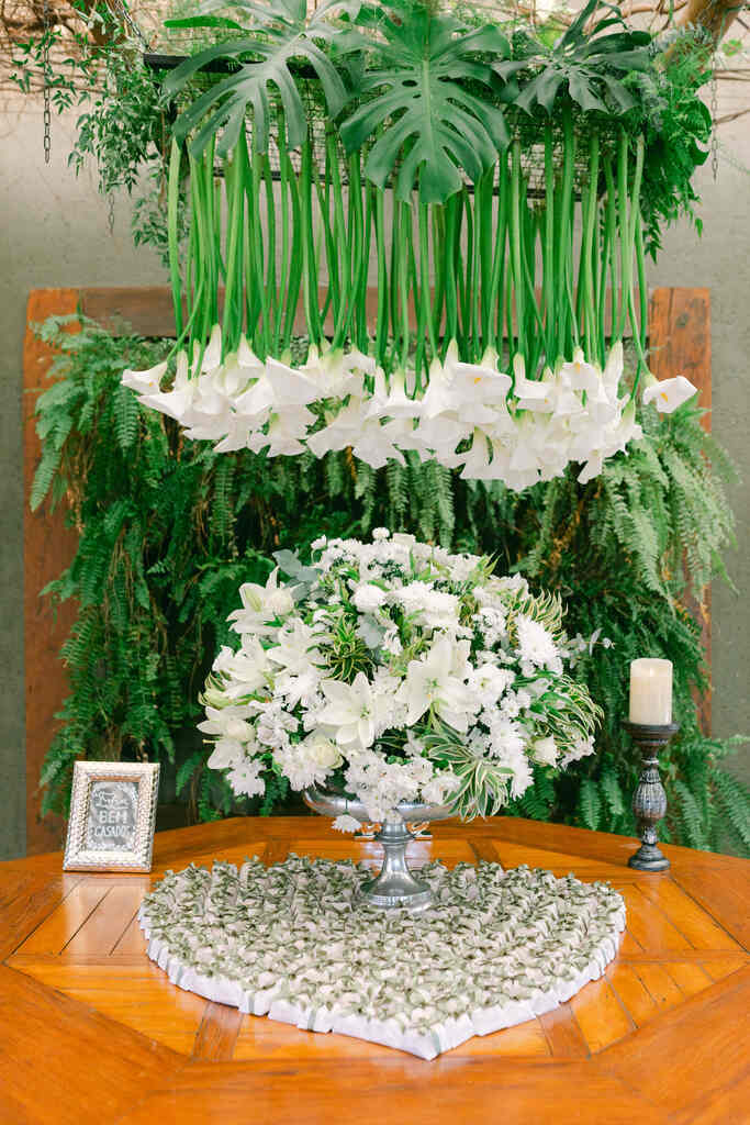mesa com bem-casados e grande arranjo de flores no centro e arranjo com tulipas e costela de adão pendentes